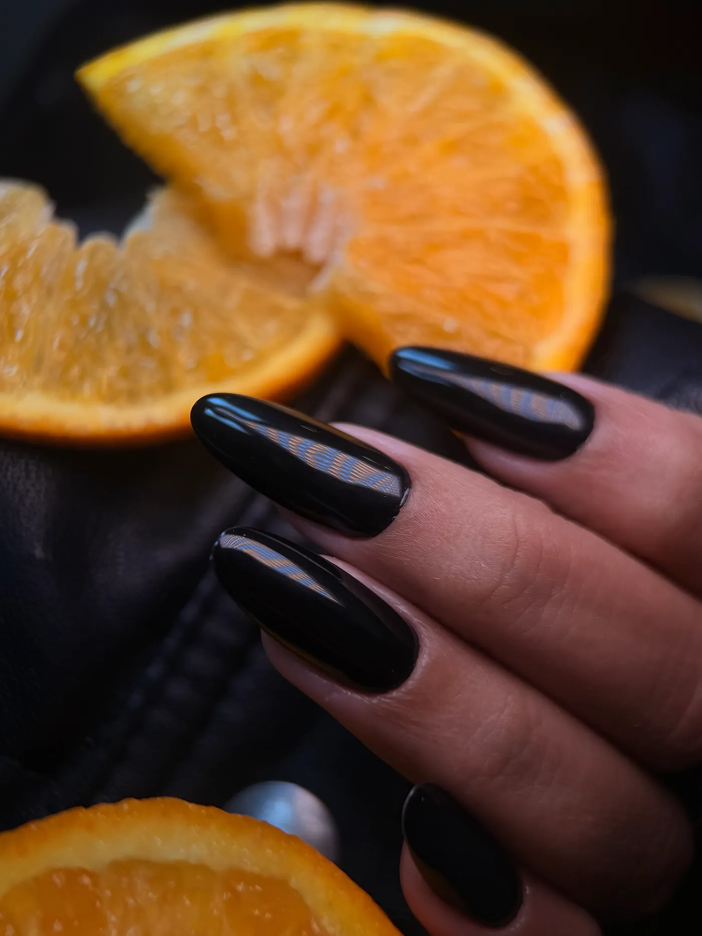 Unhas pretas brilhantes com composição de laranjas ao fundo